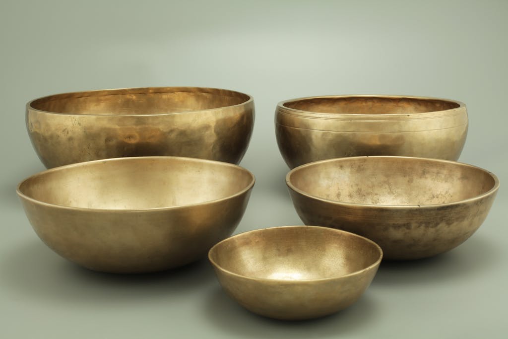 Five antique brass singing bowls on a neutral gray background, creating a serene atmosphere.