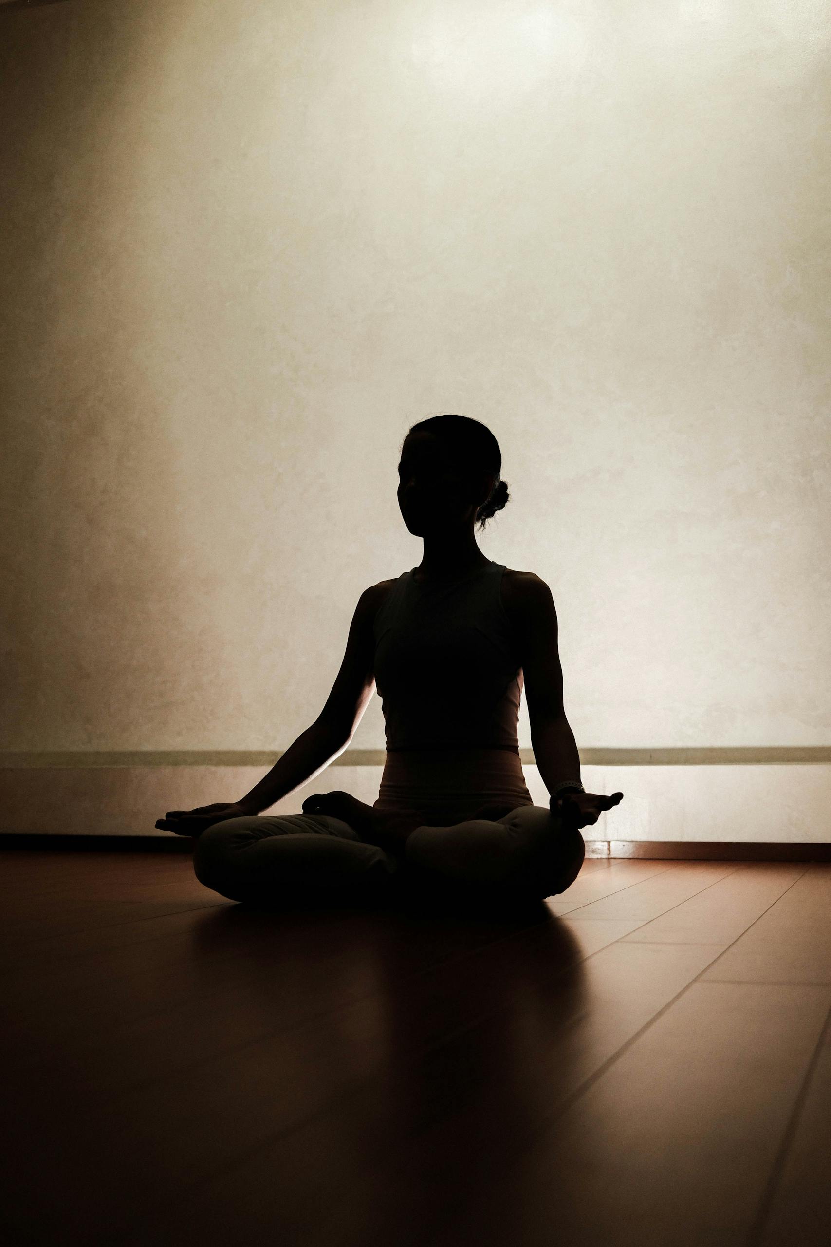 Silhouette of a person meditating in a serene indoor setting, capturing tranquility.